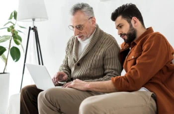 an adult male and his father look at a laptop.