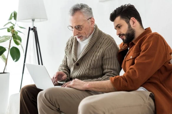 an adult male and his father look at a laptop.