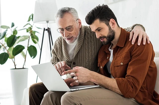 an older father and son look at something on a laptop.