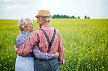 an affectionate senior couple enjoys a summer day while looking at a vast field.