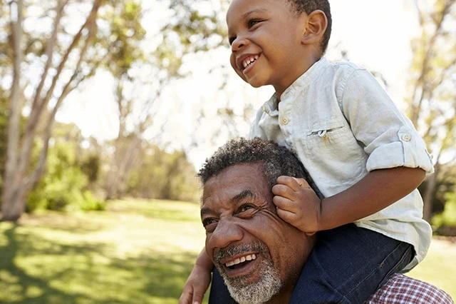 a grandfather holds his grandson on his shoulders.