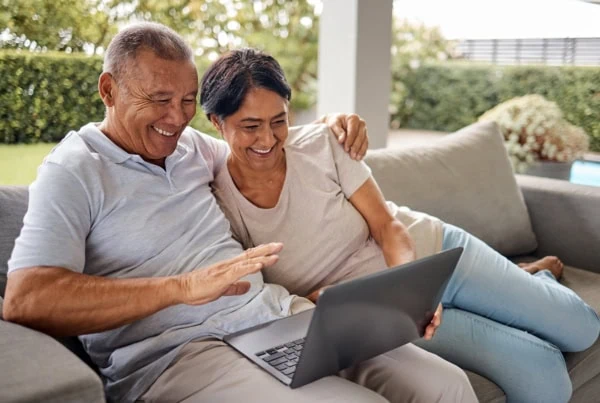 an older couple smile while looking at a laptop.