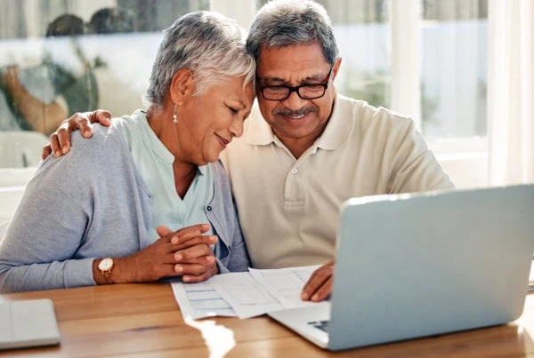 a senior woman nuzzling up to her husband as they go over financial documents.