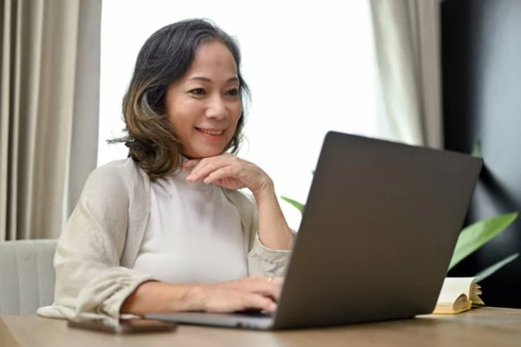 a middle-aged woman smiles while viewing her laptop.