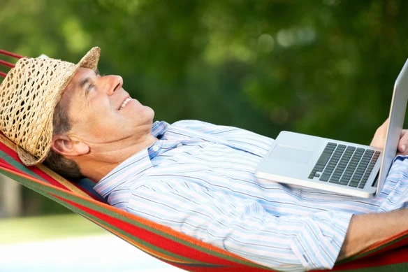 a man relaxes in a hammock with his laptop resting on his stomach.