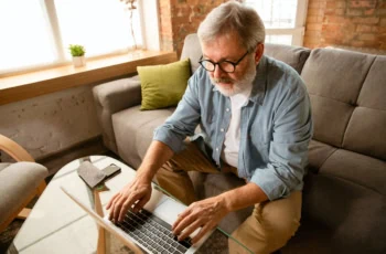 An older man is looking at his laptop while sitting on a couch.