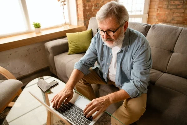 An older man is looking at his laptop while sitting on a couch.
