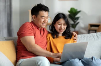 an asian couple smiles while looking at their laptop.