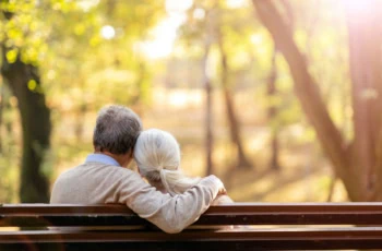 a senior couple cuddles on a park bench.