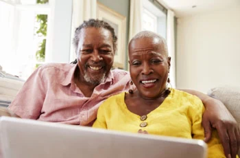 a smiling senior couple use their laptop while sitting on a sofa.