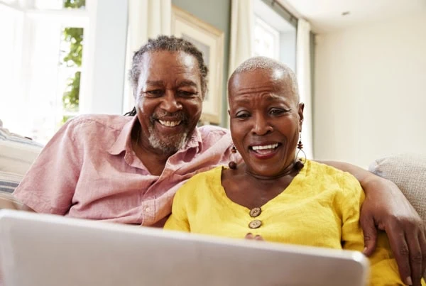 a smiling senior couple use their laptop while sitting on a sofa.