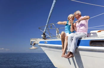 an older couple sits on the edge of a boat smiling at one another.
