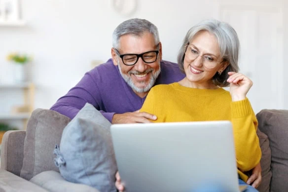a senior couple smiles while they look at a laptop.