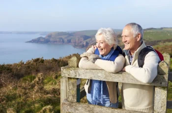 a senior couple stands on a wooden perch and looks at the coastline during the fall season.
