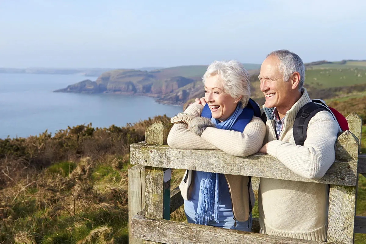 Anxious About Retirement? Here's 10 Ways to Ease Your Fears 2 a senior couple stands on a wooden perch and looks at the coastline during the fall season.