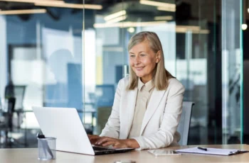 a businesswoman looks at her laptop while working in a glass building.