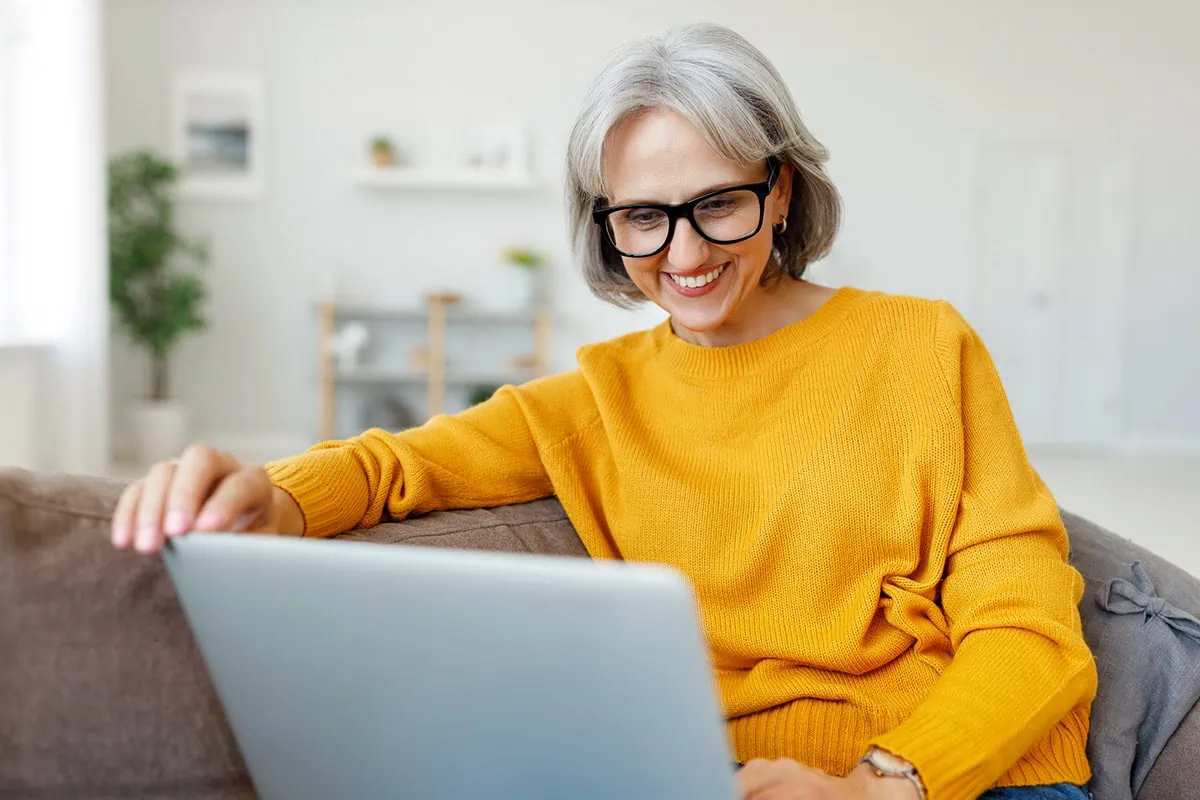 Portrait of happy smiling senior woman resting relaxing on sofa with laptop at home.