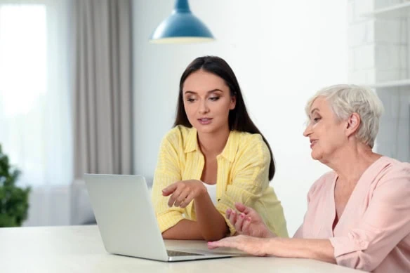a young adult looks at her laptop with her senior mother.
