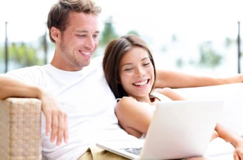 a younger couple smiles while looking at a laptop.