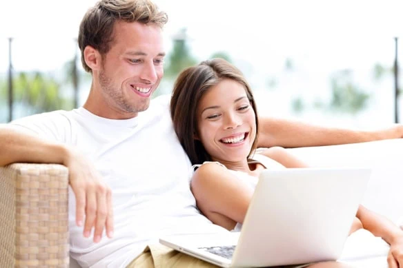 a younger couple smiles while looking at a laptop.