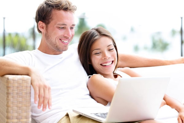 a younger couple smiles while looking at a laptop.