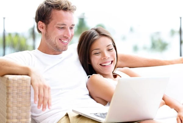 a younger couple smiles while looking at a laptop.