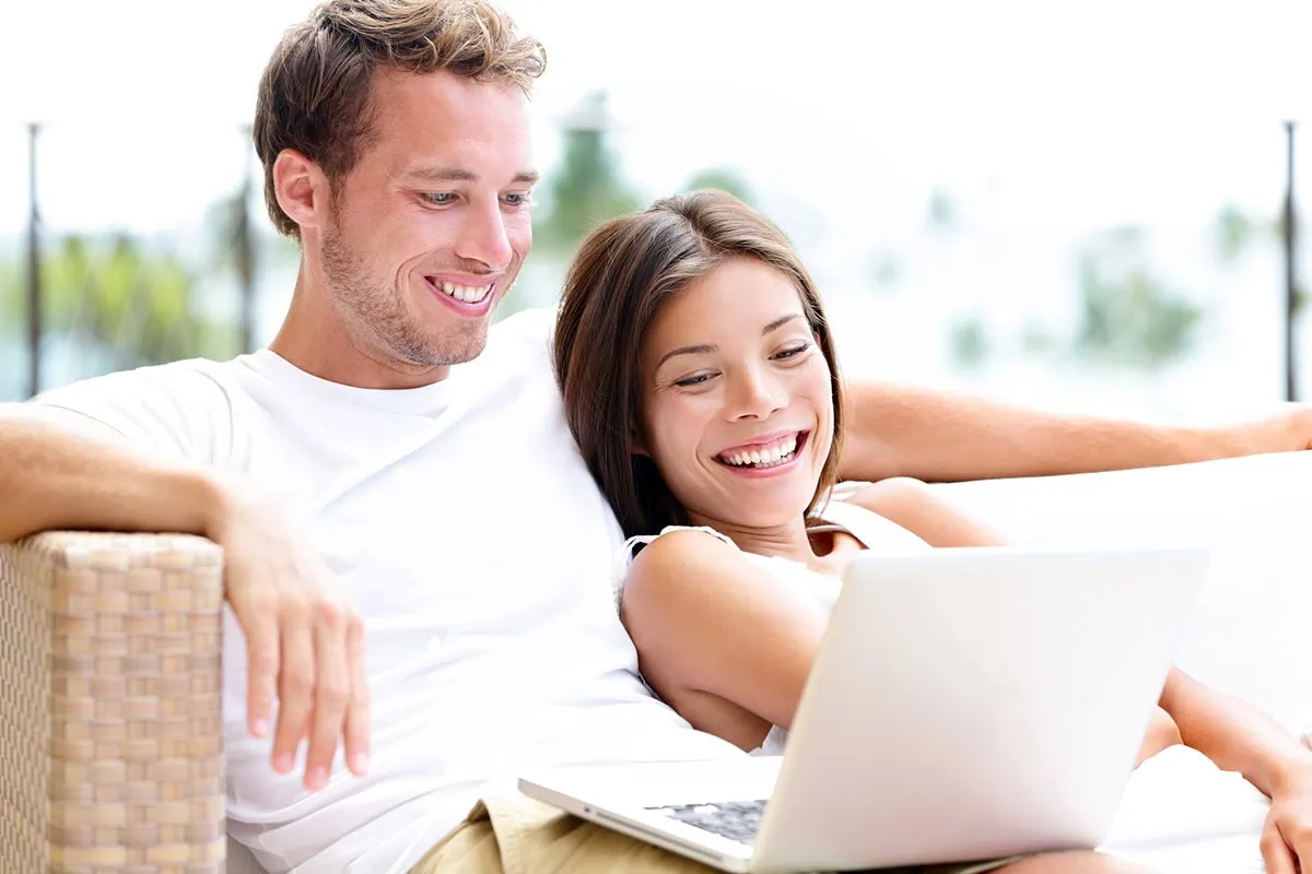 a younger couple smiles while looking at a laptop.