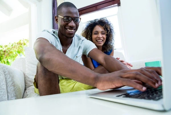 a young adult couple smiles while they use their laptop.