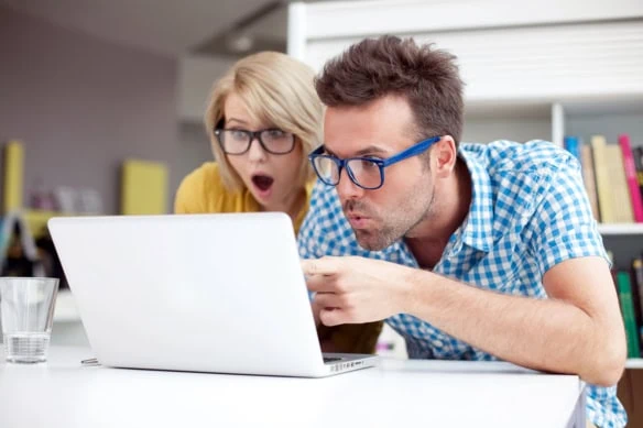 The Millennial retirement reality check: 14 key metrics to measure Millennials' retirement readiness 1 a young adult couple look surprised as they point at a laptop.