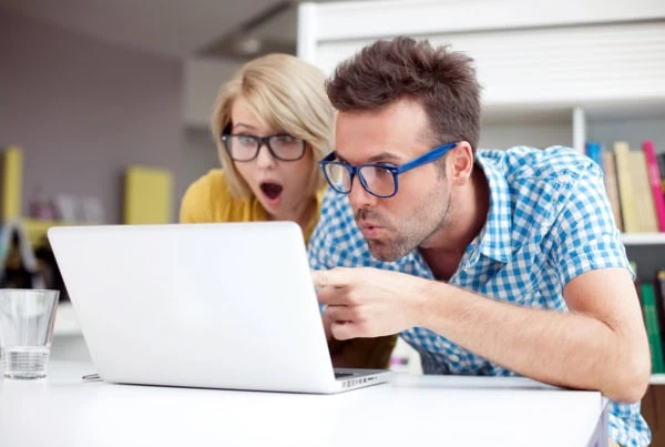 a young adult couple look surprised as they point at a laptop.