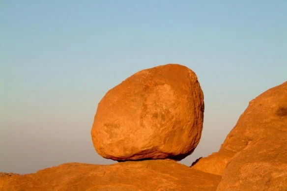 huge granite boulder perched on rocks against blue sky