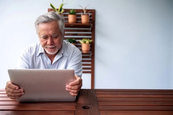 An older man adjusts the monitor portion of his laptop.