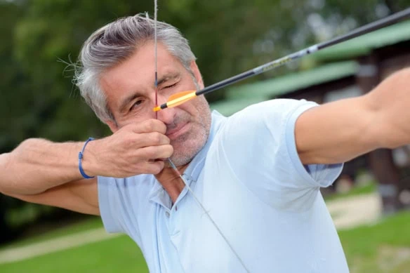 a middle-aged man pulls back an arrow on a bow.
