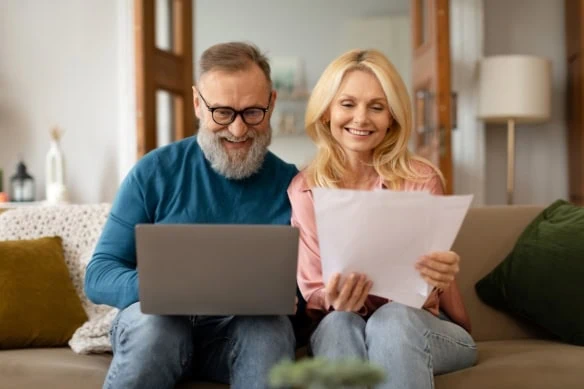 senior couple looking at financial statements and computer together on couch happy