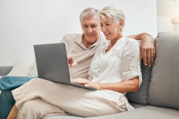 Senior, couple and online shopping with laptop on sofa in home living room with ecommerce, promotion or online deal. Old people, search and shop on internet with computer in lounge together