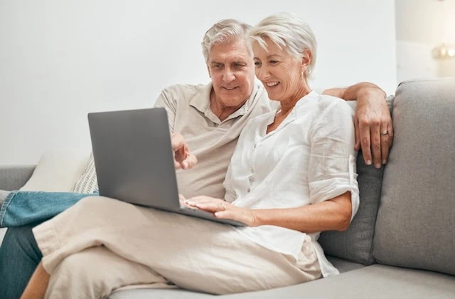 Senior, couple and online shopping with laptop on sofa in home living room with ecommerce, promotion or online deal. Old people, search and shop on internet with computer in lounge together