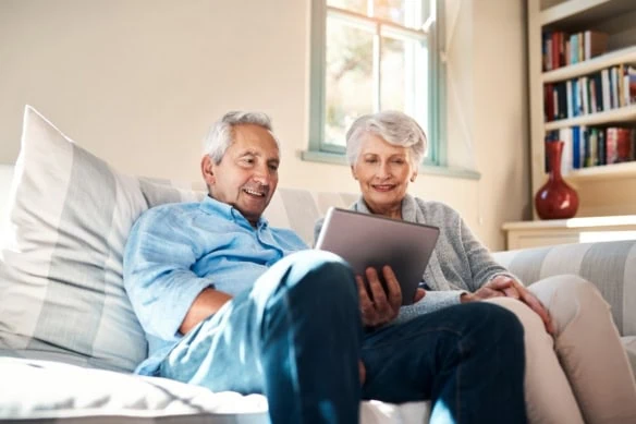 A senior couple using a digital tablet together in their living room at home.