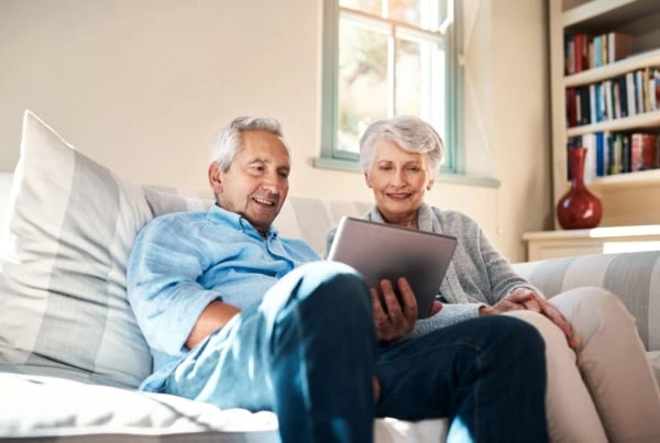A senior couple using a digital tablet together in their living room at home.