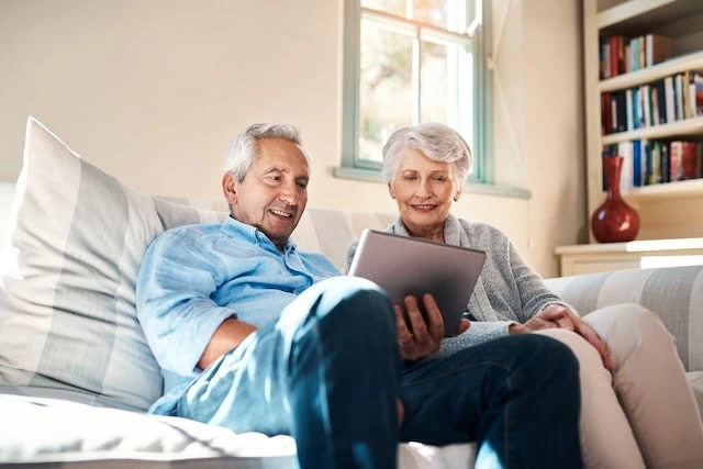 A senior couple using a digital tablet together in their living room at home.