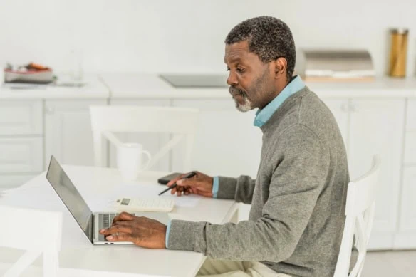 senior man looking at laptop and calculator with pen and paper