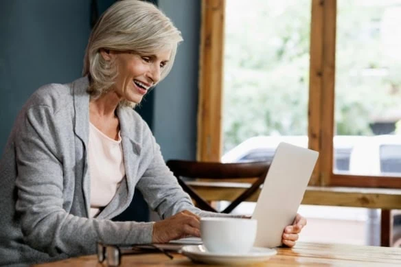 senior woman happily looking at laptop with coffee in the foreground