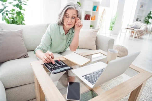 senior woman using calculator at laptop reviewing numbers