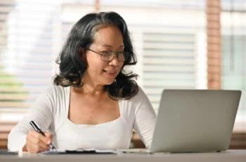 Senior woman reading online news, browsing internet on laptop at home. Retired lifestyle