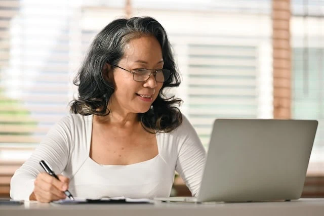 Senior woman reading online news, browsing internet on laptop at home. Retired lifestyle