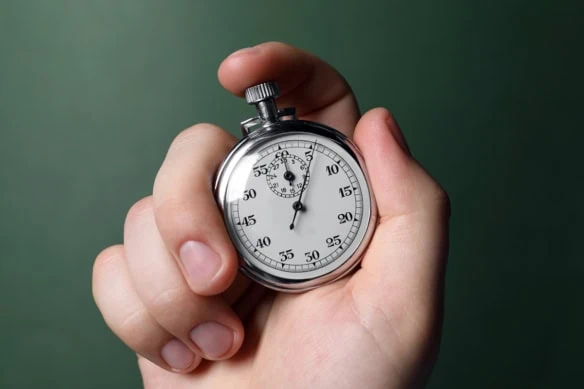 a person holds a stopwatch against a green background.