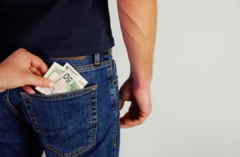 The woman pulls money out of the back pocket of the standing man's blue jeans. Close-up view of the hands.