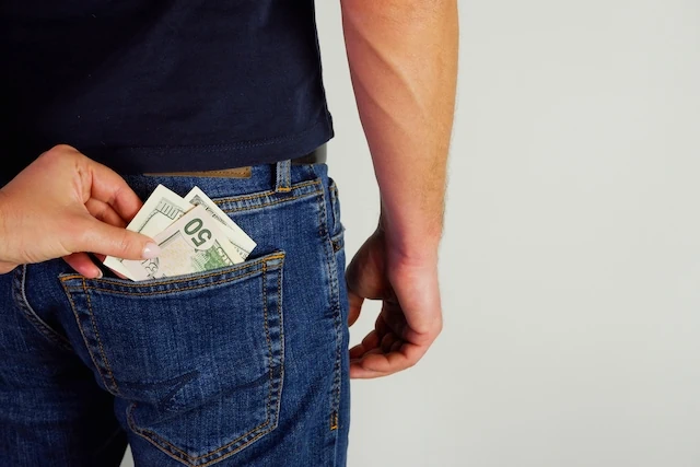 The woman pulls money out of the back pocket of the standing man's blue jeans. Close-up view of the hands.