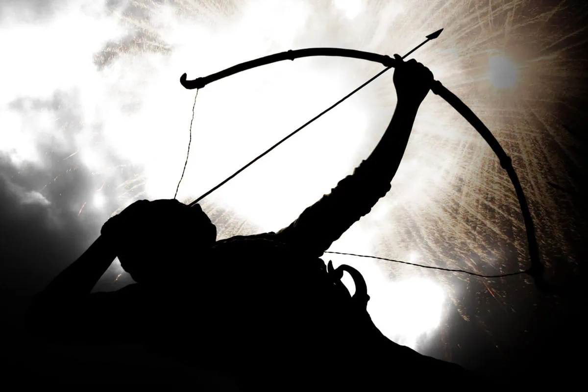 A silhouette of an archer against a cloudy sky.