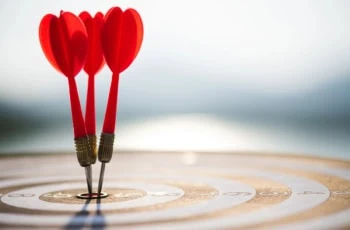 three arrows have hit the bullseye on a target resting on the ground.