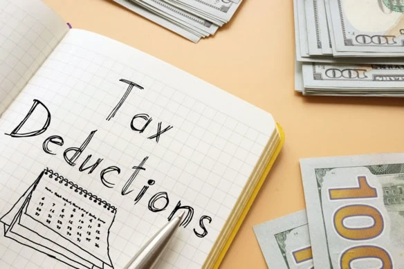 the words tax deductions are written on a notepad sitting on a table with many hundred dollar bills.